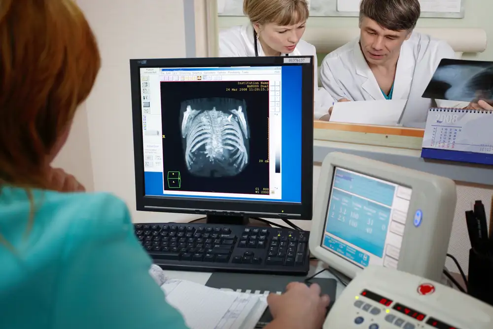 Doctors reviewing spinal X-ray and taking notes on a clipboard while planning disc replacement surgery in a hospital.